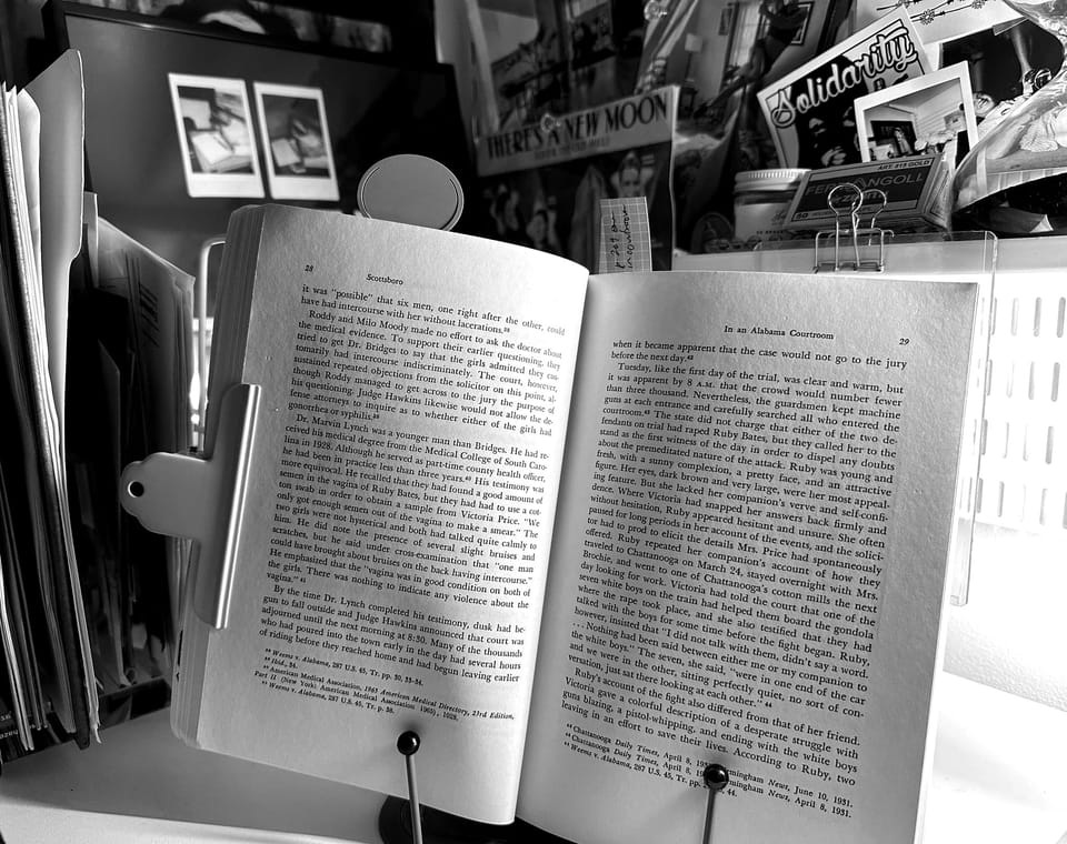 A book open on a stand, on my desk, surrounded by photos and ephemera