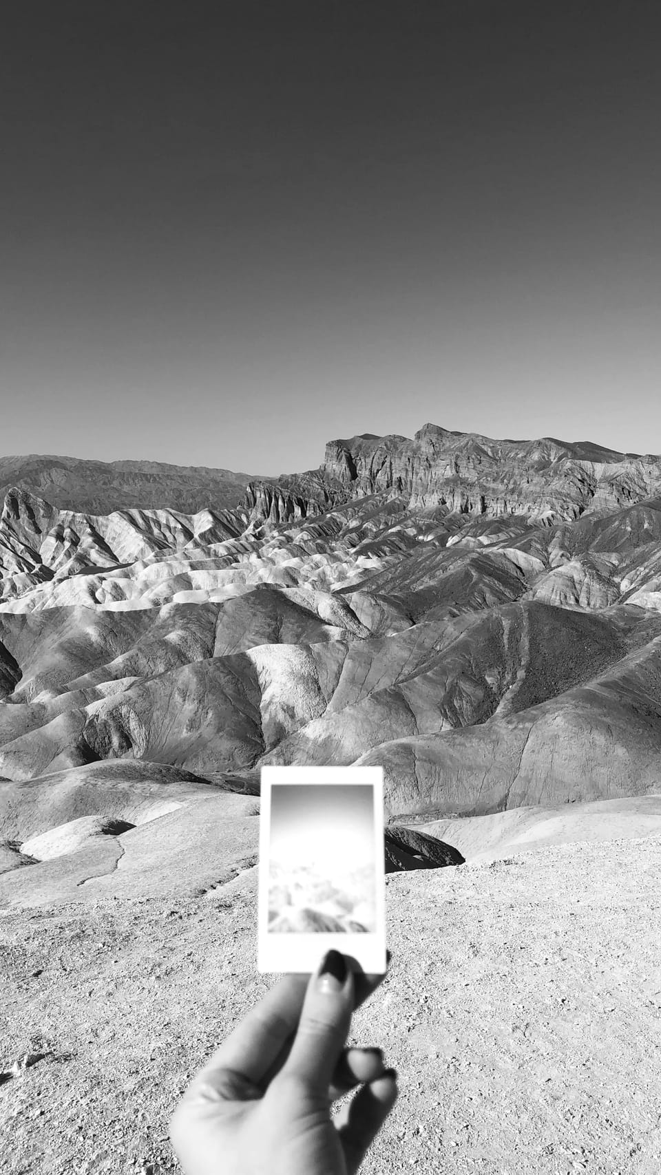 a hand in the foreground holds a photo of Death Valley, against the background of Death Valley