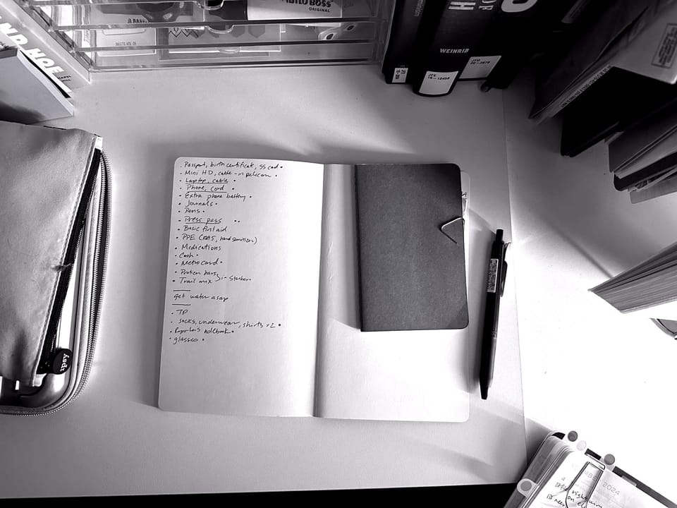 An open notebook on my desk, with a handwritten list of go-bag items, framed by books.